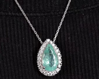 May include: A silver chain necklace with a pear-shaped emerald gemstone pendant surrounded by smaller diamonds.