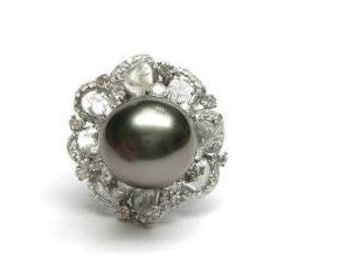 Pode incluir: Um anel de prata com uma pérola preta e um design floral com diamantes menores.
