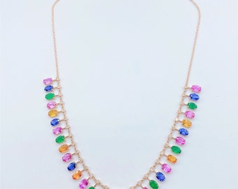 May include: A delicate gold necklace with a chain and a row of colorful oval gemstones. The gemstones are arranged in a rainbow pattern, with blue, green, yellow, pink, and orange stones.