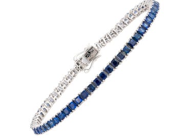 May include: A tennis bracelet featuring a row of square-cut, deep blue gemstones set in a silver-toned metal. The bracelet is clasped and displayed against a white background, showcasing its elegant design. The gemstones are a vibrant blue.