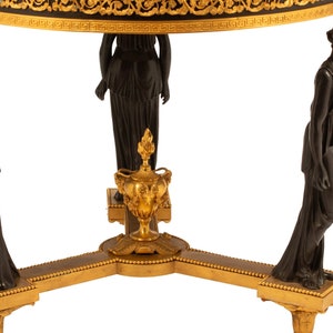 May include: A black and gold table with three legs, each featuring a bronze statue of a woman. The table top has a black and gold design.
