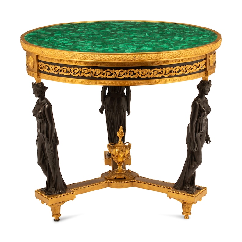 May include: A round, green malachite table top with gold accents and a black and gold base with three legs, each featuring a bronze sculpture of a woman.