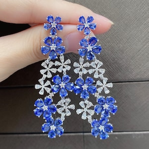 May include: A pair of drop earrings featuring a cascade of blue sapphire and white diamond flowers. The earrings are made of silver and have a delicate, feminine design.
