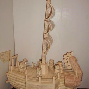 May include: A detailed ivory carving of a ship with a tall mast and multiple sails. The ship has a carved figurehead and a crew of figures on deck. The ship is on a black base.