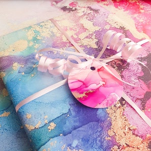 May include: A gift wrapped in blue, pink and gold marbled paper with a pink ribbon and a pink and gold circle tag.