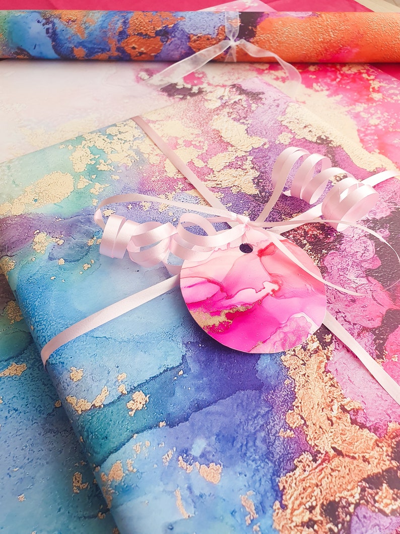 May include: A gift wrapped in blue, pink and gold marbled paper with a pink ribbon and a pink and gold circle tag.