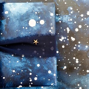 May include: A wrapped gift with a dark blue and white speckled design, resembling a starry night sky. A dark blue ribbon with a gold star charm is wrapped around the gift. The background has a similar design.