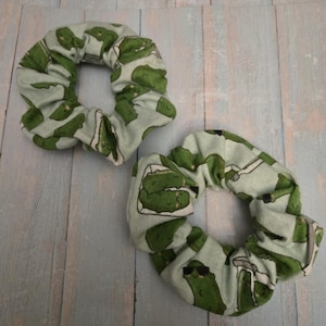 May include: Two green and white scrunchies with a pickle print. The pickles are wearing sunglasses.