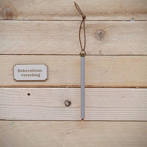 May include: A wooden sign with the text "Dekorations-vorschlag" hanging from a brown leather cord on a light wood background.