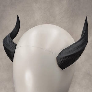 Könnte beinhalten: Ein weißer Mannequin-Kopf mit schwarzen Teufelshörnern, die oben angebracht sind.