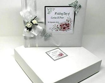 May include: White wedding photo album with a silver ribbon and a white bow with a small flower embellishment. The album cover has a silver border with the text "Wedding Day of Carina & Peter 7th September 2019".