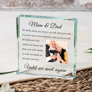 May include: A clear glass block with a photo of an older couple holding glasses of wine. The text "Mum & Dad" is at the top of the block, and the text "We think about you always, we talk about you still. You have never been forgotten, and you never will. We hold you close within our hearts and there you will remain, to walk and guide us through our lives, Until we meet again" is printed below the photo.