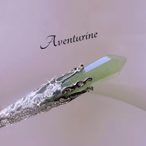 May include: Aventurine crystal wand with a silver-colored metal filigree design. The green crystal is faceted and pointed. The word "Aventurine" is written in cursive.