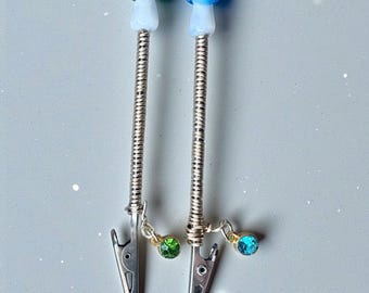 May include: Two silver-toned hair clips with mushroom-shaped toppers. One mushroom is green and white, the other is blue and white. Each clip has a dangling charm with a gemstone, one green and one blue.