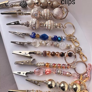 May include: A collection of beaded ATM clips in various designs. The clips feature gold-toned metal clasps and are adorned with an assortment of beads in colors like gold, pearl, pink, and blue. The text "Mystery ATM clips" is visible.