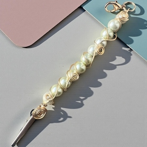 May include: A pearl beaded accessory with a gold-colored metal clip and clasp. The pearls are strung together with gold wire in a spiral pattern. The clip is silver-colored.