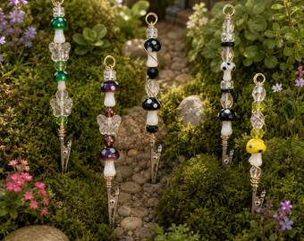 May include: Five vertical metal clips featuring decorative beaded stems with glass mushroom charms in green, purple, black, white, and yellow, accented with clear faceted beads and butterfly-shaped glass spacers, each topped with a small metal ring.