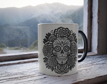 May include: White ceramic mug with a black handle. The mug features a black and white illustration of a sugar skull surrounded by flowers.