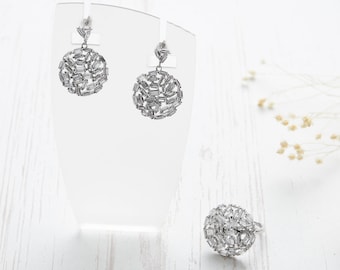 Puede incluir: Un conjunto de pendientes y un anillo de plata con un diseño redondo adornado con piedras transparentes en forma de baguette.