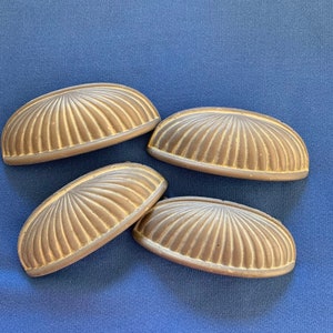 May include: Four antique brass cabinet pulls with a fluted design. The pulls are arranged in a semi-circle on a blue background.