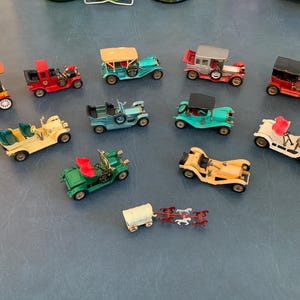 May include: A collection of vintage toy cars in various colors, including red, yellow, green, and blue. Some cars have open tops, while others have enclosed cabins. A small wagon pulled by toy horses is also present.