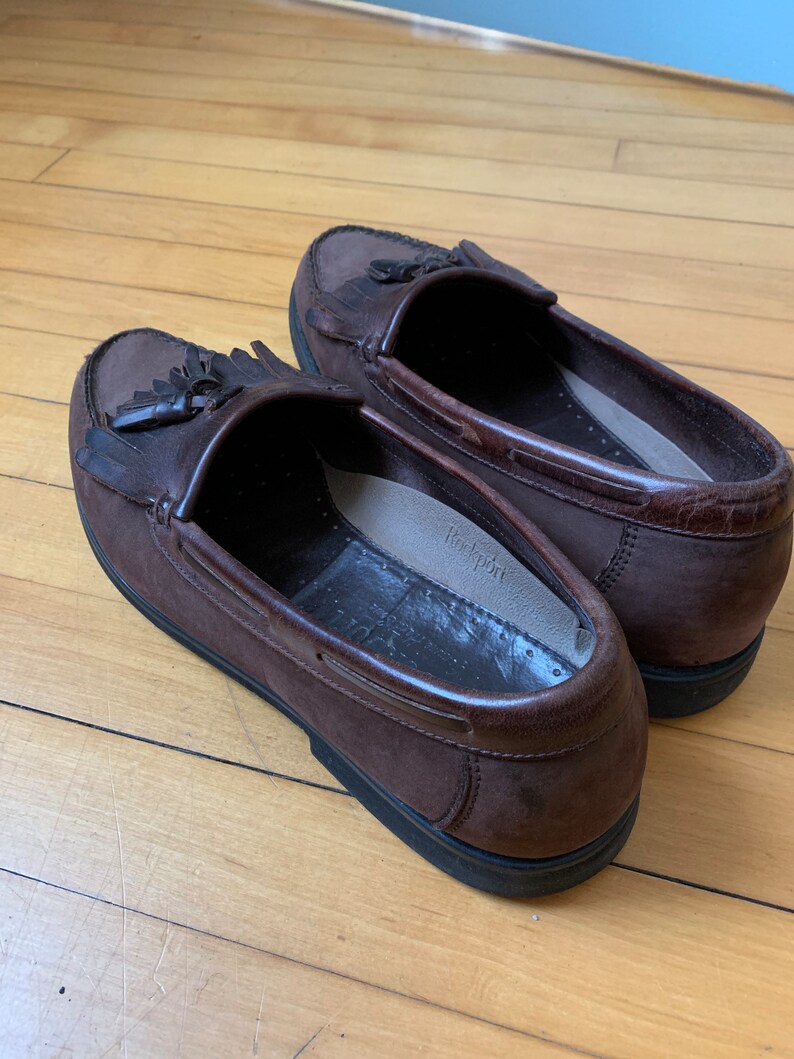 Peut inclure: Une paire de mocassins &agrave; franges en cuir marron avec une semelle en caoutchouc noir. Les mocassins ont une doublure en cuir marron et une semelle int&eacute;rieure blanche avec le mot "Rockport" imprim&eacute; dessus.
