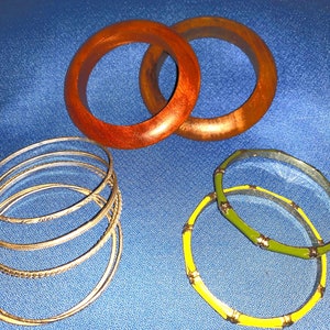 May include: A set of six bracelets, including two wooden bangles, three silver-toned bangles, and one green and yellow bangle.