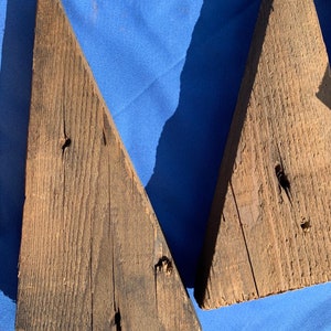 May include: Two triangular pieces of weathered wood with a dark brown color. The wood has a rough texture and is showing signs of age.
