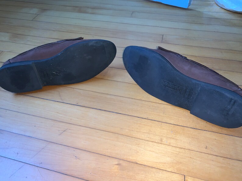 Peut inclure: Une paire de mocassins en cuir marron avec des semelles en caoutchouc noir. Les semelles ont un motif textur&eacute;.