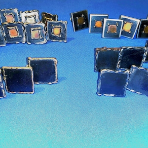 May include: A collection of small, square, metal tiles with various colors and patterns. The tiles have a rustic, hand-crafted look and are arranged in a grid pattern.