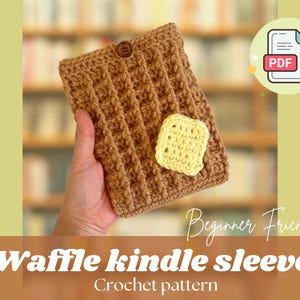 May include: A brown crocheted Kindle sleeve with a waffle stitch pattern. The sleeve has a yellow crocheted button and a small yellow crocheted flower on the front. The text "Beginner Friendly" and "Waffle Kindle Sleeve Crochet pattern" is printed below the image.