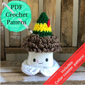 May include: Crocheted elf hat with brown hair and a white collar, sitting on a white mug with a smiling face. The mug is on a wooden surface. The text "Includes: Collar coaster pattern!" is in red on a white background.