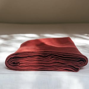 Peut inclure: Un drap en lin bordeaux plié sur un couvre-lit blanc.