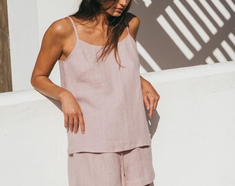 Puede incluir: Una mujer lleva un top de tirantes de lino rosa y pantalones cortos a juego. El atuendo es de estilo relajado y casual, perfecto para el clima cálido.