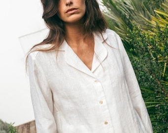 May include: A white linen shirt with a collared neckline and long sleeves. The shirt has a button-up front and is made of a lightweight, breathable fabric.