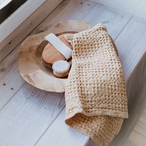 Op de afbeelding: Een houten kom met twee borstels van natuurlijke haren en een witte washandje op een wit houten oppervlak.