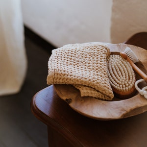 Op de afbeelding: Een houten kom met een beige gebreide washandje en een houten borstel met natuurlijke haren.