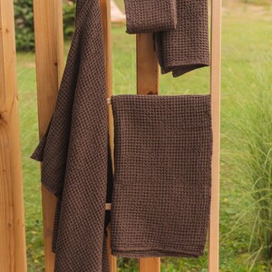 Op de afbeelding: Vier bruine wafeldoek handdoeken hangen aan een houten rek. De handdoeken zijn van verschillende grootte en zijn allemaal gemaakt van een zacht, absorberend materiaal.