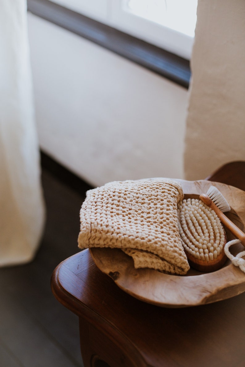 Op de afbeelding: Een houten kom met een beige gebreide washandje en een houten borstel met natuurlijke haren.