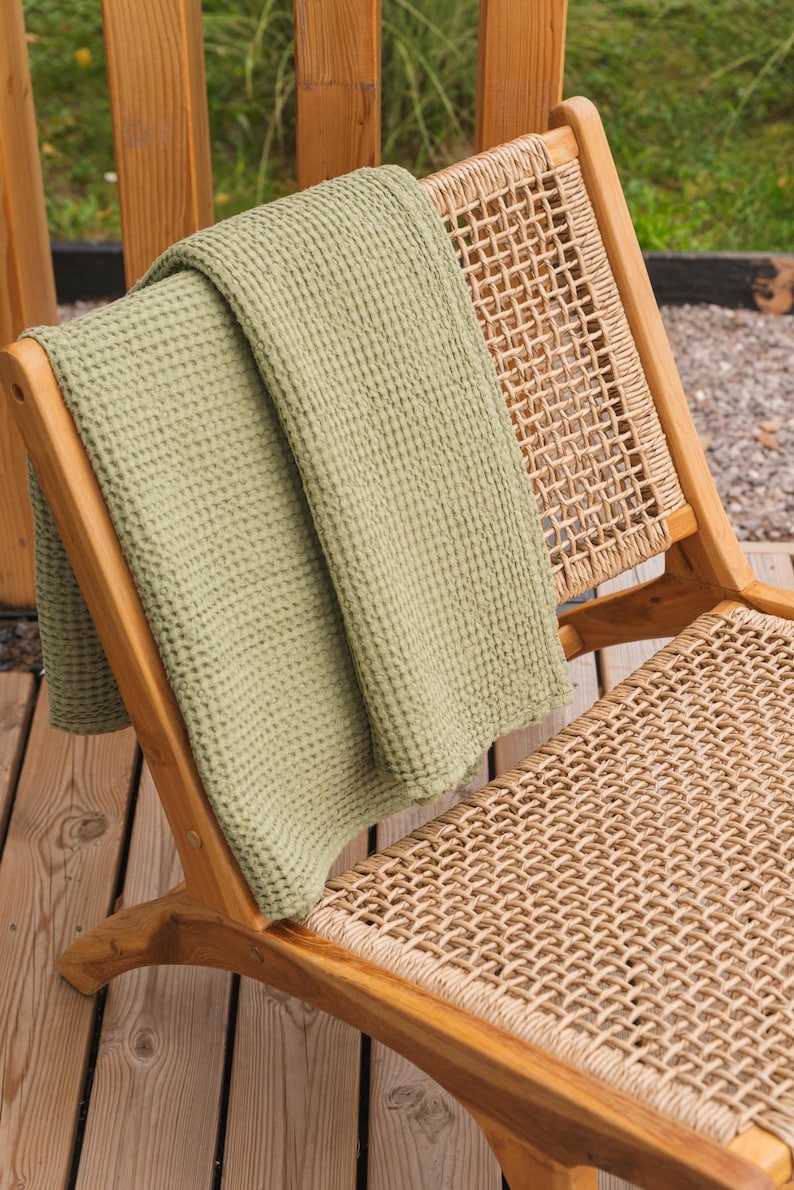 Op de afbeelding: Een groene wafelstructuur deken gedrapeerd over een houten stoel met een gevlochten rieten zitting.