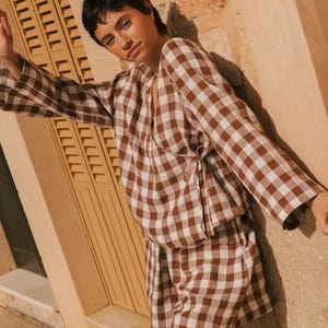 K&ouml;nnte beinhalten: Ein braunes und wei&szlig;es Gingham-Wickeltop und passende Shorts. Das Oberteil hat einen V-Ausschnitt und lange &Auml;rmel. Die Shorts sind hoch tailliert und haben eine lockere Passform.