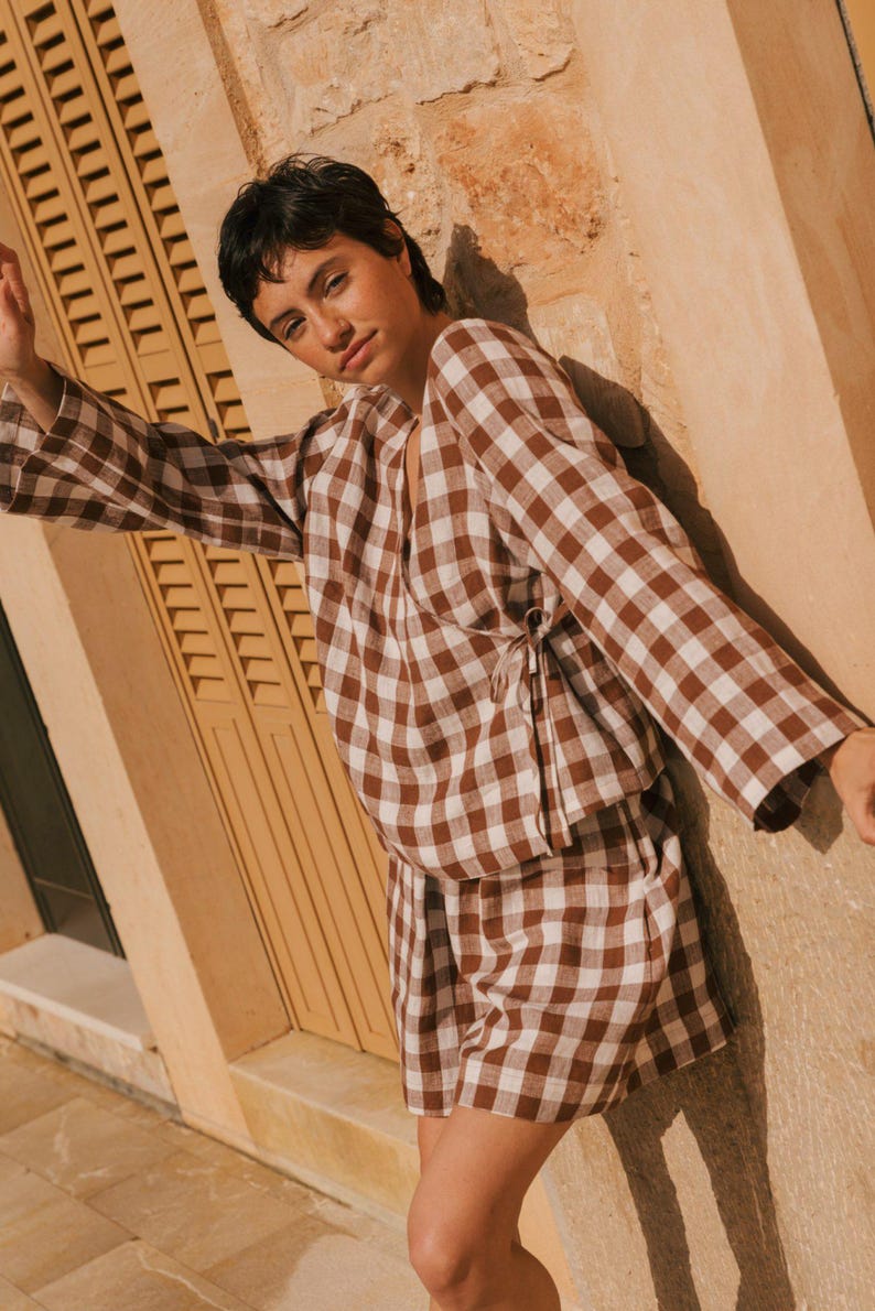 K&ouml;nnte beinhalten: Ein braunes und wei&szlig;es Gingham-Wickeltop und passende Shorts. Das Oberteil hat einen V-Ausschnitt und lange &Auml;rmel. Die Shorts sind hoch tailliert und haben eine lockere Passform.