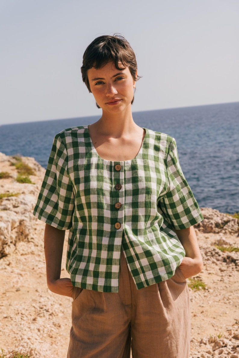 May include: A green and white gingham button-up shirt with short sleeves. The shirt is made of a lightweight fabric and has a relaxed fit.