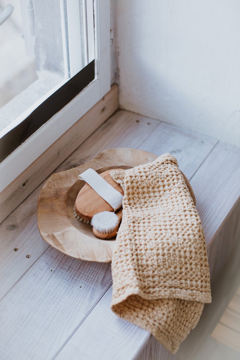 Op de afbeelding: Een houten kom met twee borstels van natuurlijke haren en een witte washandje op een wit houten oppervlak.