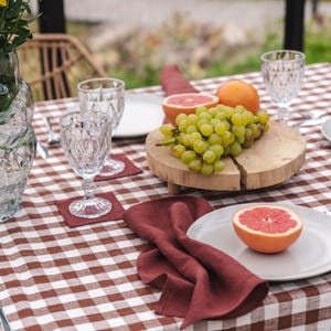 May include: A brown and white checkered tablecloth with a red linen napkin, a plate with a grapefruit half, and a wooden cutting board with grapes and grapefruit halves.