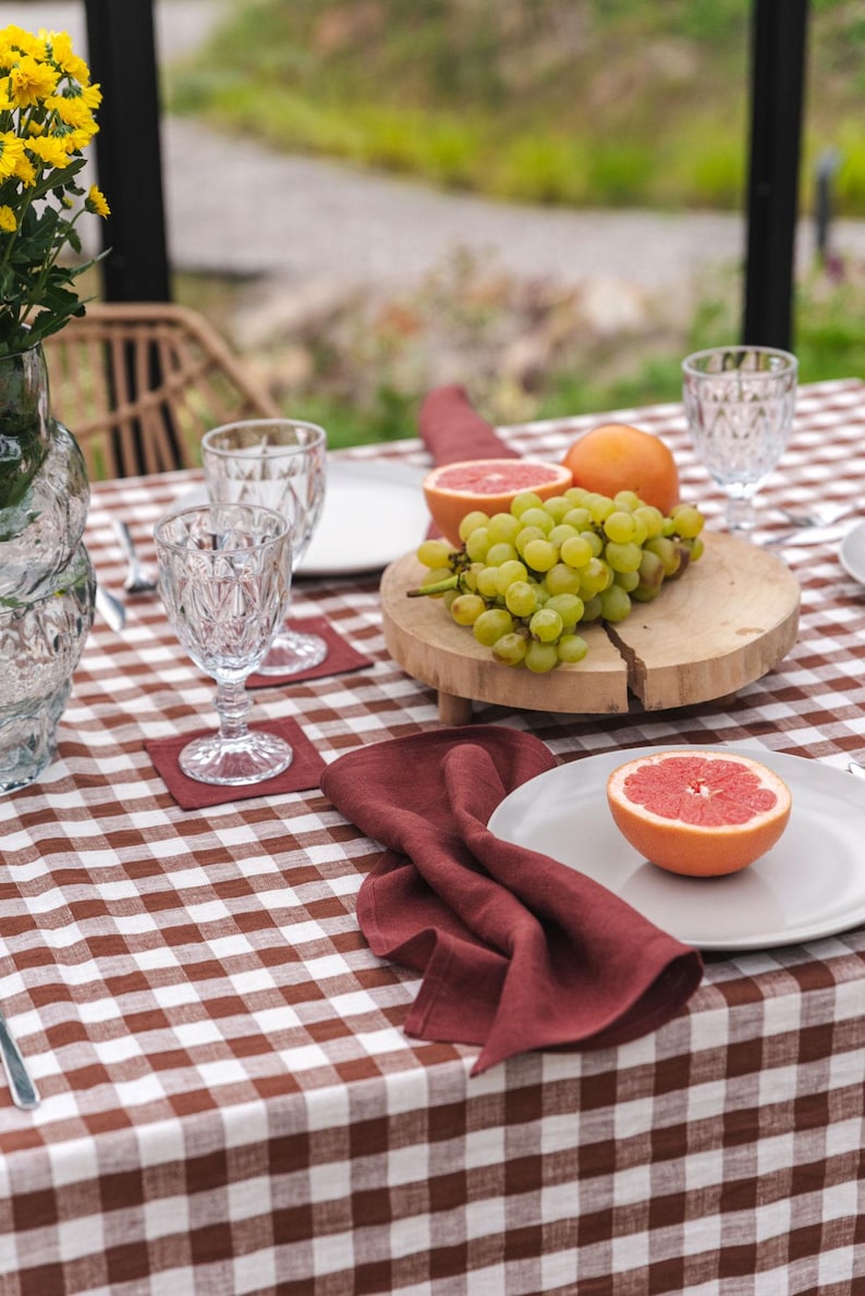 May include: A brown and white checkered tablecloth with a red linen napkin, a plate with a grapefruit half, and a wooden cutting board with grapes and grapefruit halves.