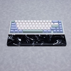 May include: A white and light blue mechanical keyboard with a black and white marble patterned wrist rest. The keyboard has a green space bar and blue keys for the function row.