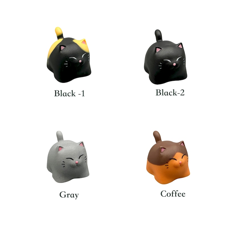 May include: Four small ceramic cat figurines in different colors: black with yellow, black, gray, and orange. Each cat has a smiling face and is sitting upright.