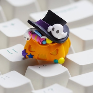 May include: A Halloween-themed keyboard keycap featuring an orange jack-o'-lantern with a black top hat and a white ghost. The pumpkin is filled with colorful candies. A fun and festive accessory for any keyboard.
