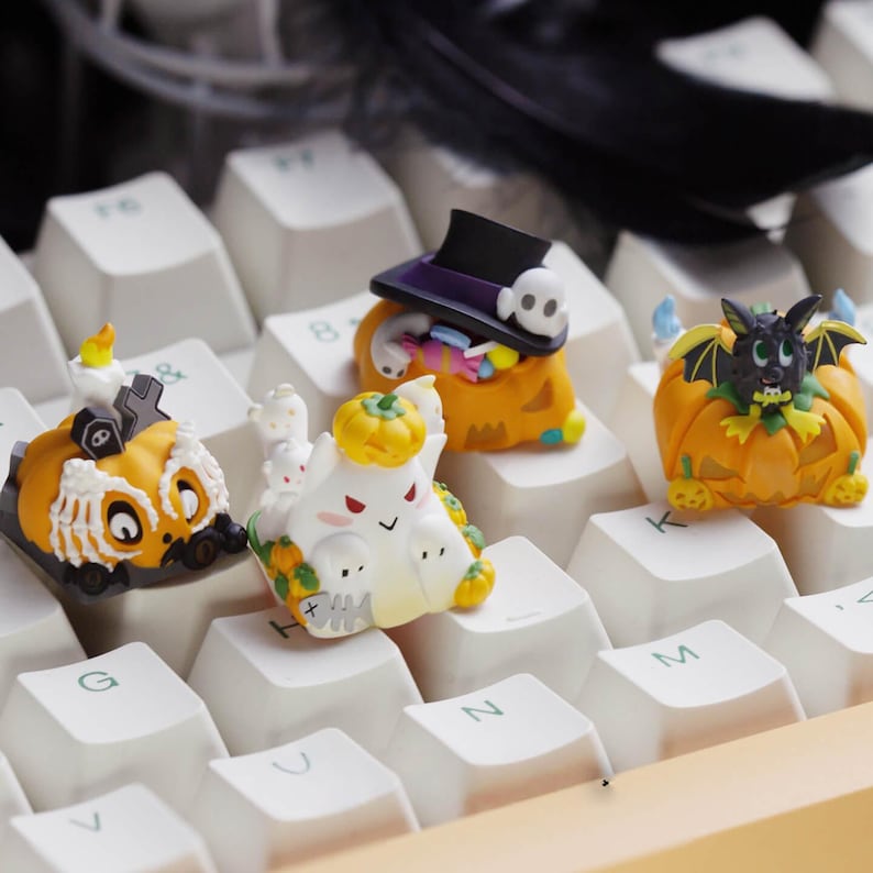 May include: A collection of Halloween-themed keyboard keycaps. The keycaps feature various designs, including a pumpkin with a bat, a ghost, a pumpkin with a hat and candy, and a pumpkin with a candle and a tombstone. The keycaps are orange, white, black, and purple.